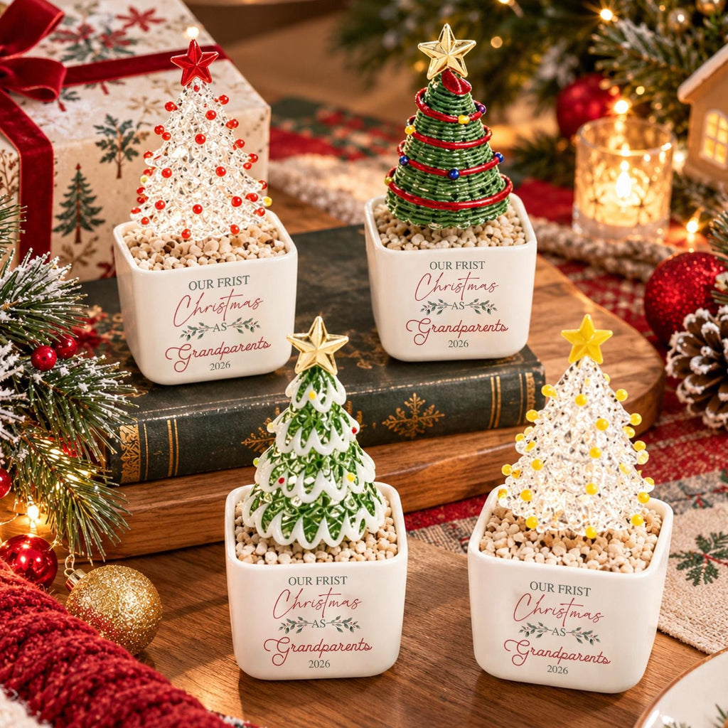 May include: Four square white ceramic planters containing decorative Christmas trees. Each planter features the text "OUR FRIST Christmas AS Grandparents 2026". The trees include a clear beaded tree with red stars, a green coiled tree, a green and white tree, and a clear beaded tree with yellow stars.