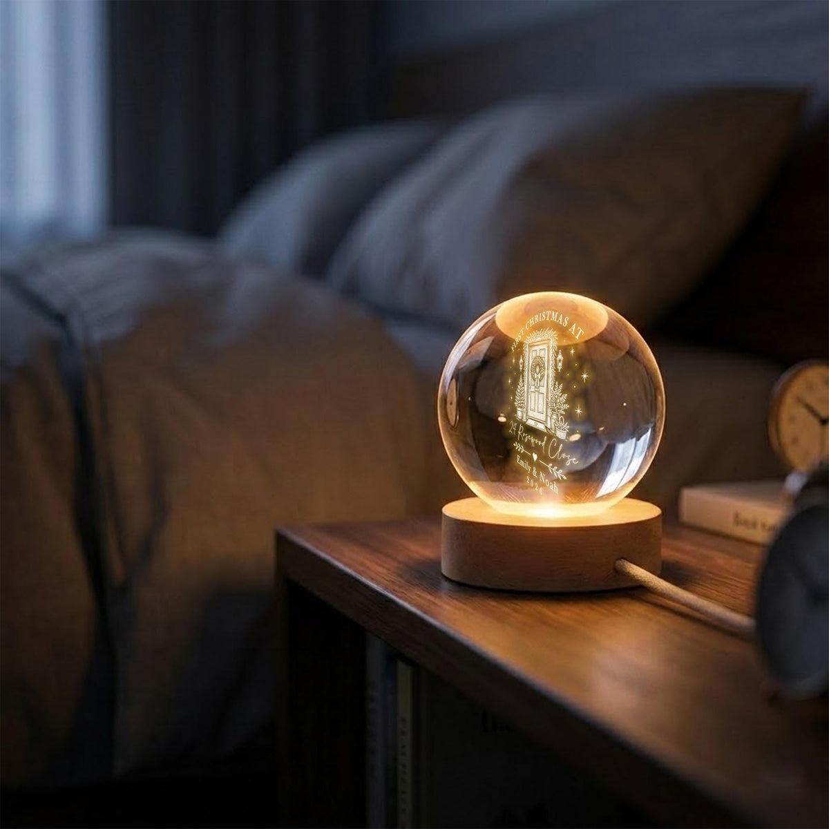 May include: A clear glass sphere lamp resting on a circular wooden base. The sphere features an internal laser-etched design of a front door with a wreath, surrounded by stars, with the text "Our Christmas at 24 Pervod Close" and names.