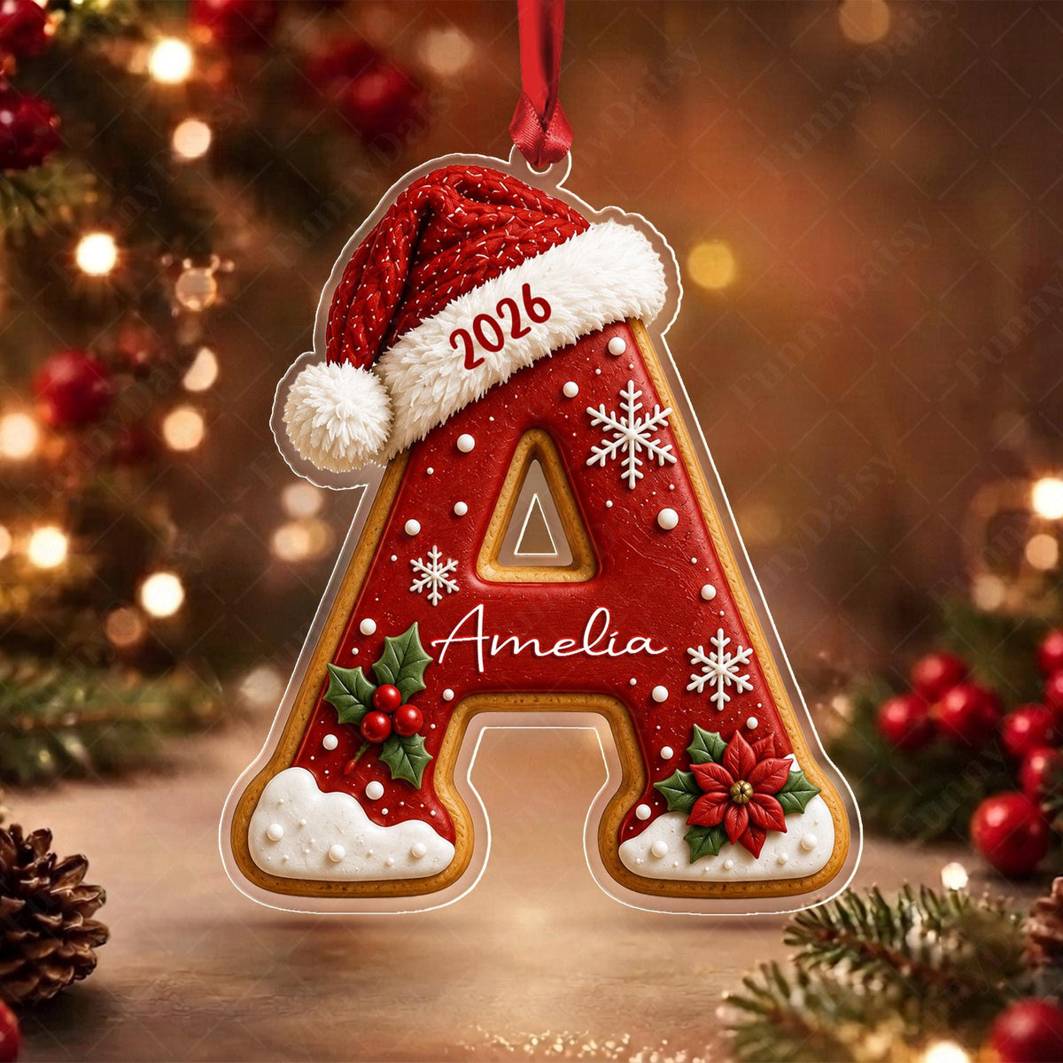 May include: A red letter A Christmas ornament shaped like a gingerbread cookie, topped with a red Santa hat. The letter features the text 2026 and the name Amelia, decorated with white snowflakes, green holly leaves, red berries, and white icing.