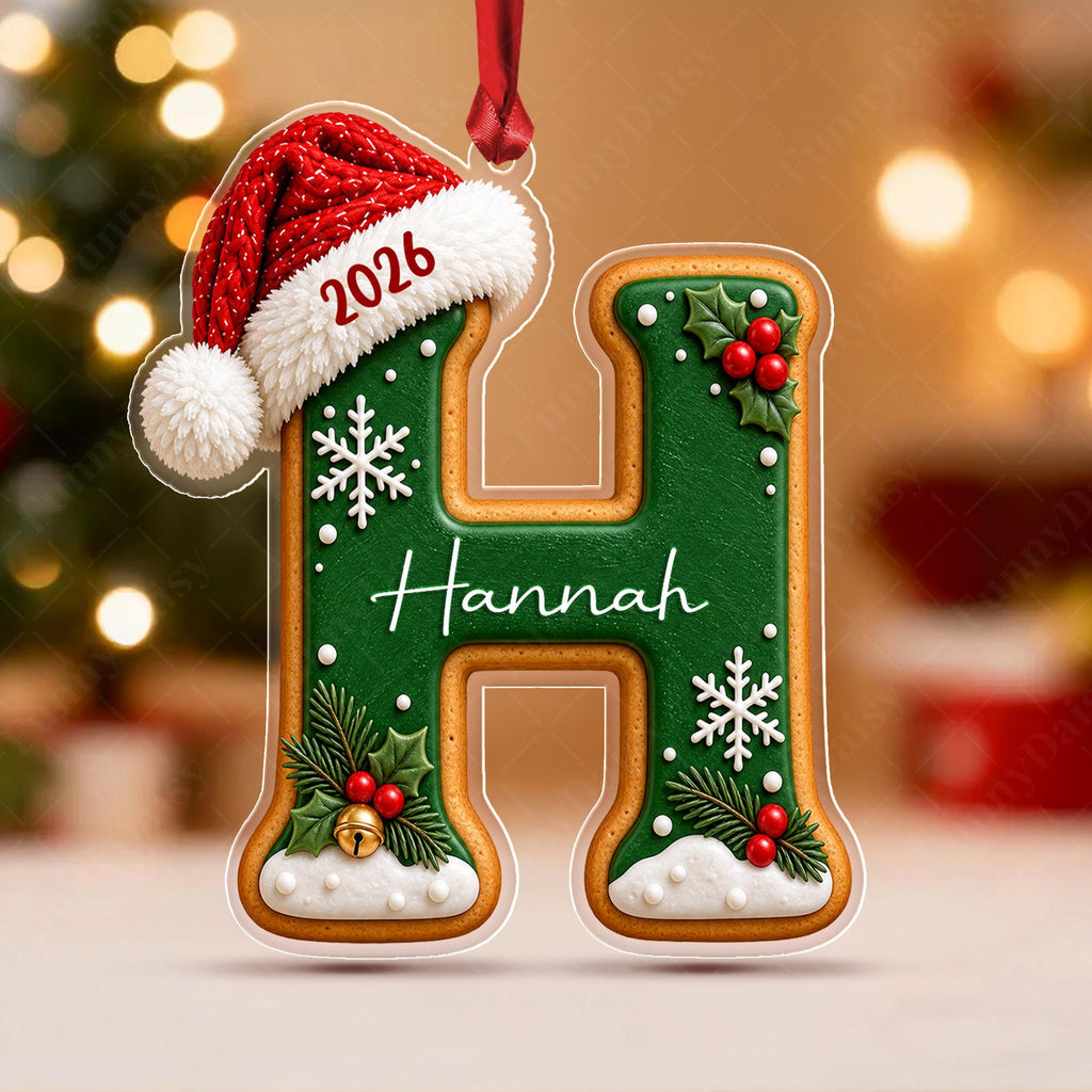 May include: A letter H Christmas ornament shaped like a gingerbread cookie with green icing, white snowflake accents, and a red Santa hat featuring the year 2026. The name Hannah is written in white script across the center, with holly and a bell.