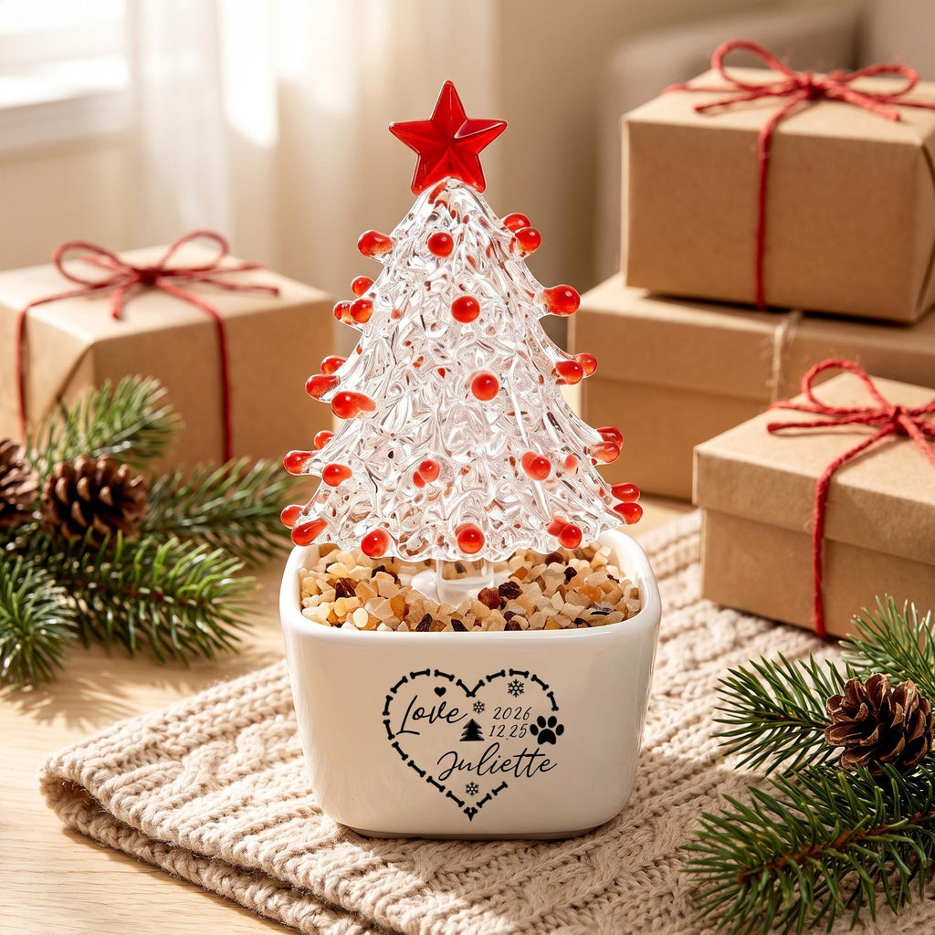 May include: A clear glass Christmas tree ornament with red glass accents and a red star topper, set in a white square ceramic planter filled with small stones. The planter features a black heart graphic with the text Love, 2026, 12 25, and Juliette.