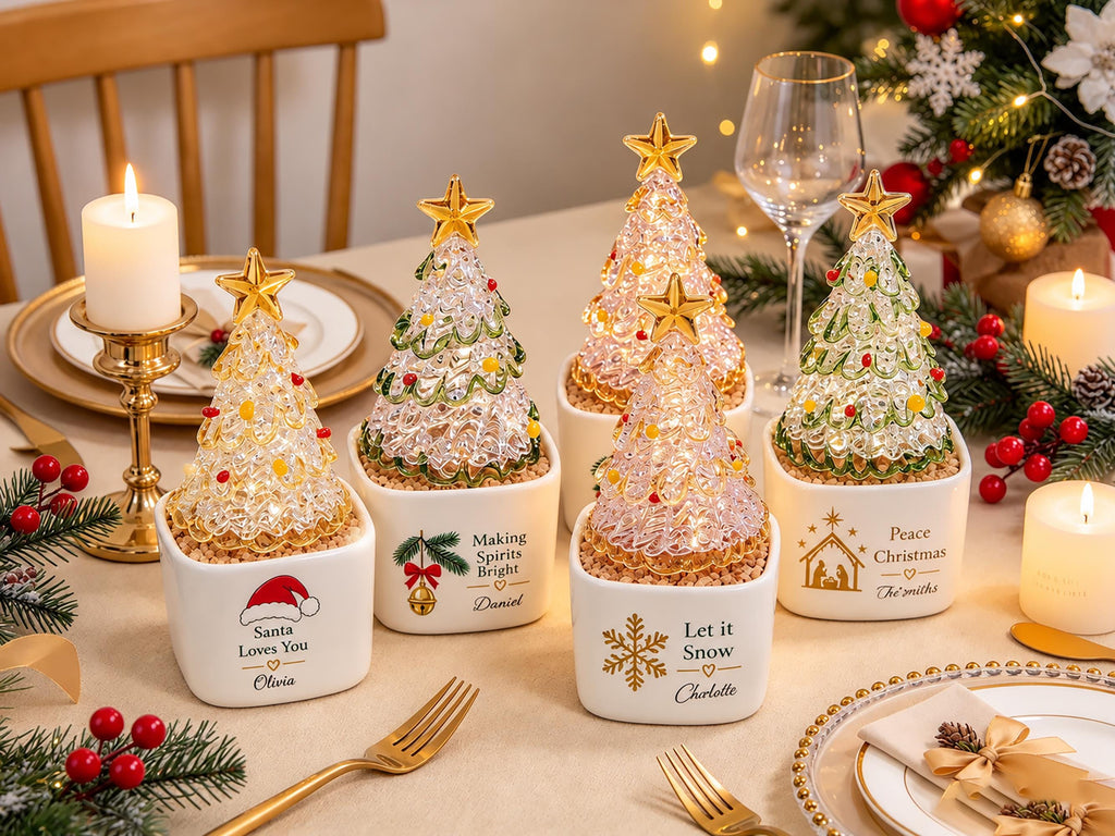 May include: Five white square ceramic planters, each containing a clear, textured glass Christmas tree topped with a gold star. The planters feature personalized holiday text and graphics, including Santa Loves You, Making Spirits Bright, Let it Snow, and Peace Christmas.