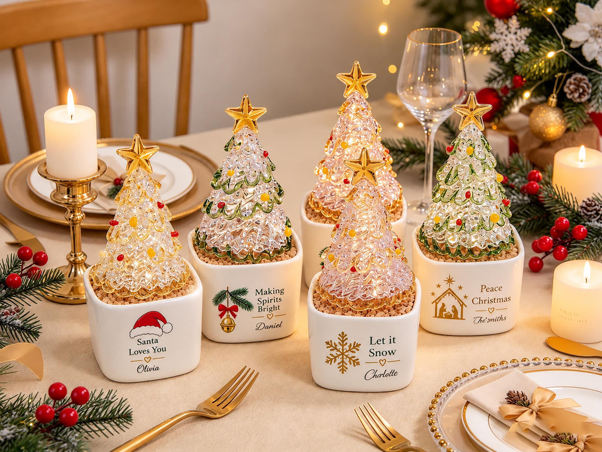 May include: Five white square ceramic planters, each containing a clear, textured glass Christmas tree topped with a gold star. The planters feature personalized holiday text and graphics, including Santa Loves You, Making Spirits Bright, Let it Snow, and Peace Christmas.