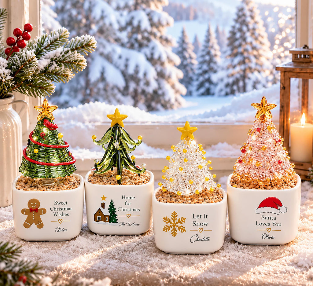 May include: Four small glass Christmas tree figurines in white square ceramic pots filled with pebbles. Each tree is topped with a yellow star and features unique decorations, including a gingerbread man, a house, a snowflake, and a Santa hat.