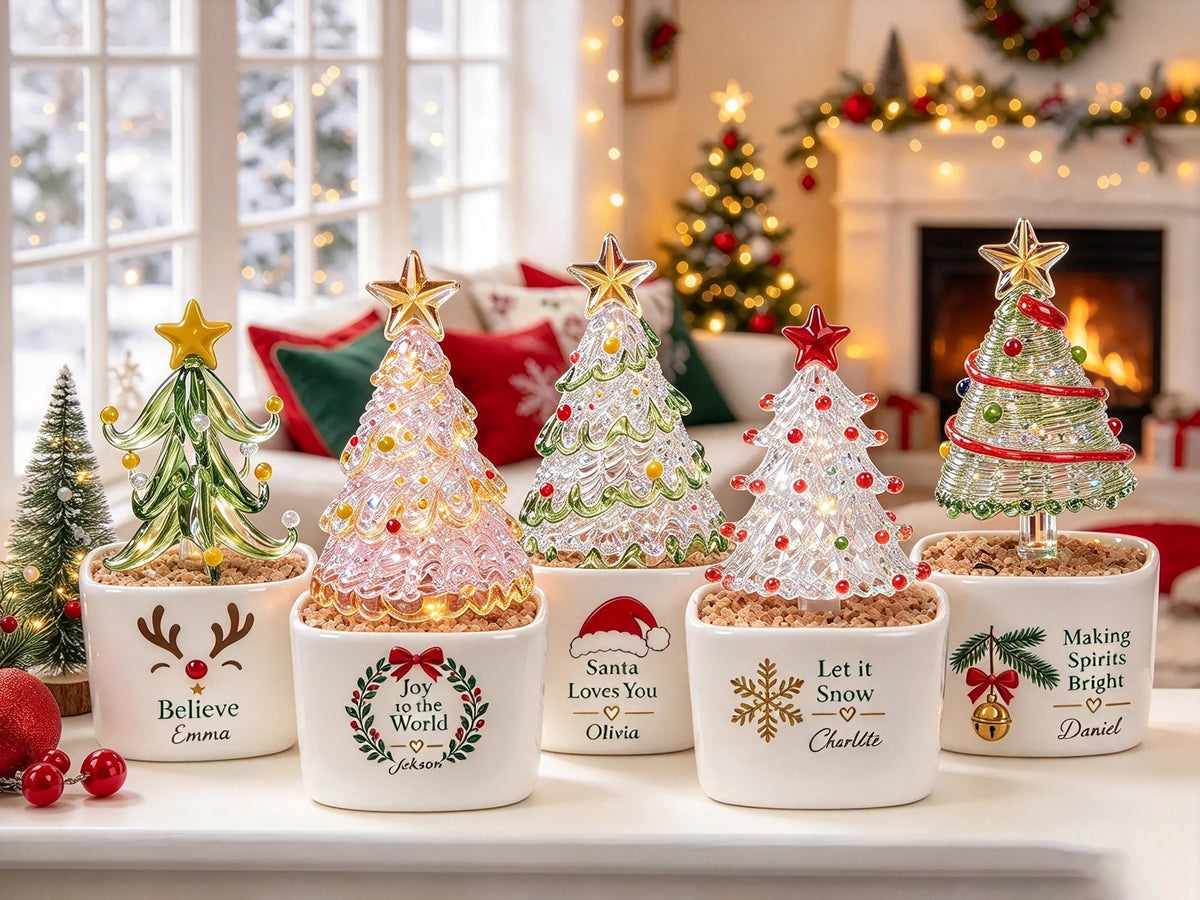 May include: Five decorative glass Christmas trees in white ceramic pots. The pots feature festive graphics and names: Believe Emma, Joy to the World Jekson, Santa Loves You Olivia, Let it Snow Charlotte, and Making Spirits Bright Daniel.