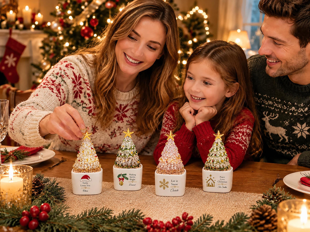 May include: Four miniature Christmas tree ornaments with gold star toppers, each set in a square white ceramic base. The bases feature festive graphics and text including Santa, mistletoe, snowflakes, and a nativity scene with personalized names.