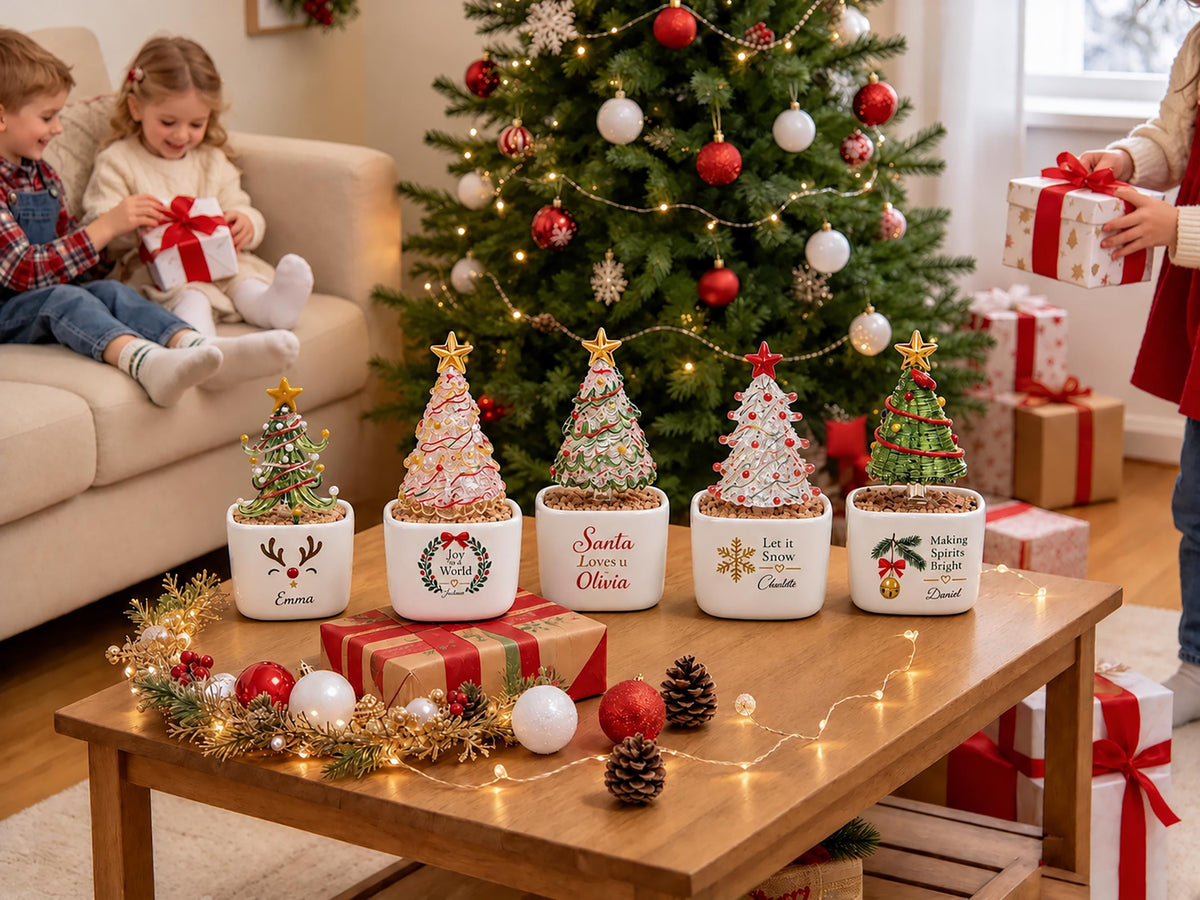 May include: Five small decorative Christmas trees in white square ceramic pots. Each tree features unique ornaments and a star topper. The pots are personalized with names and holiday phrases including Joy to the World, Santa Loves Olivia, Let it Snow, and Making Spirits Bright.