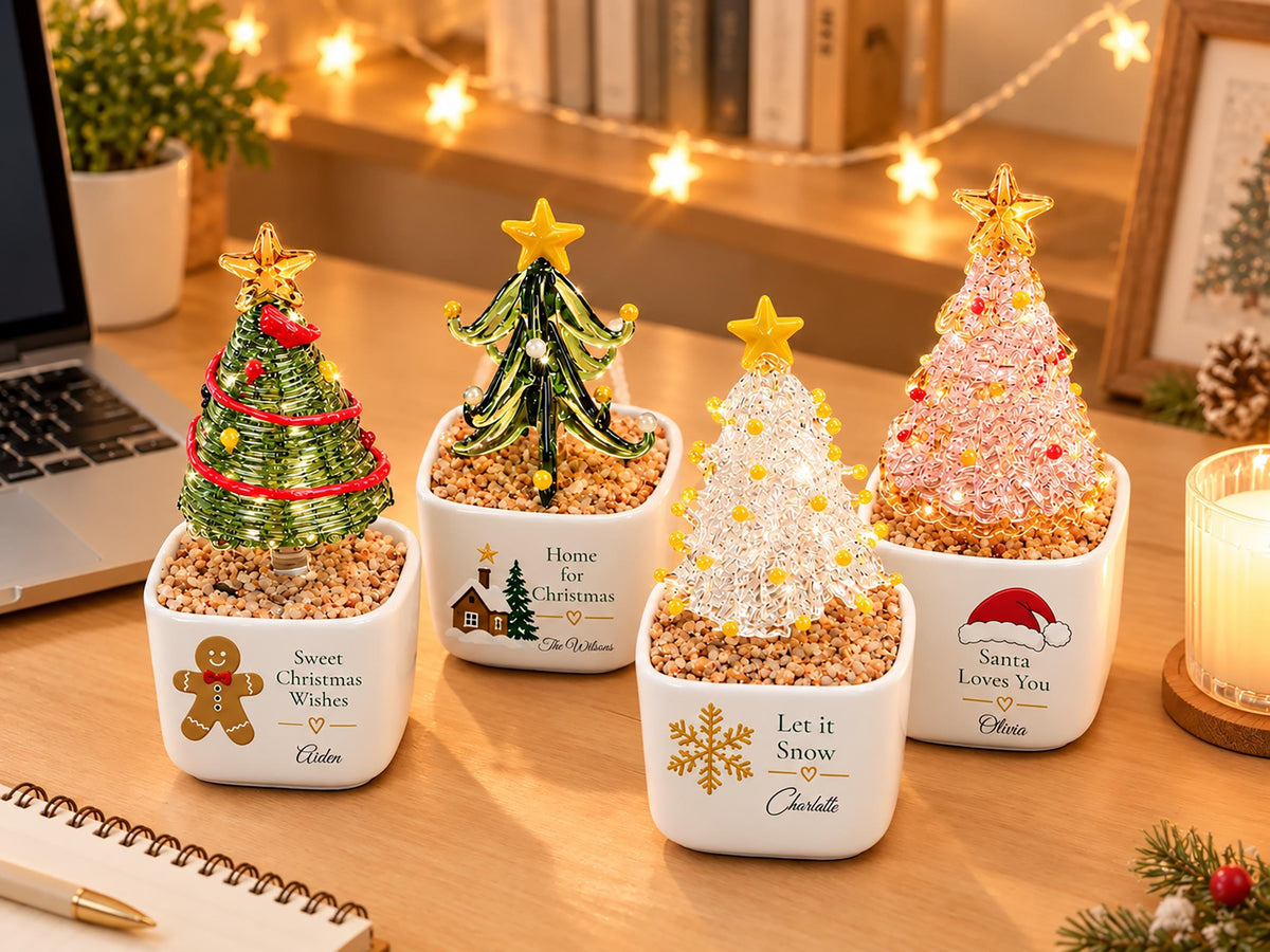 May include: Four decorative glass Christmas tree ornaments in white ceramic pots filled with small pebbles. Each tree features a yellow star topper and unique festive designs on the pots, including a gingerbread man, a house, a snowflake, and a Santa hat.