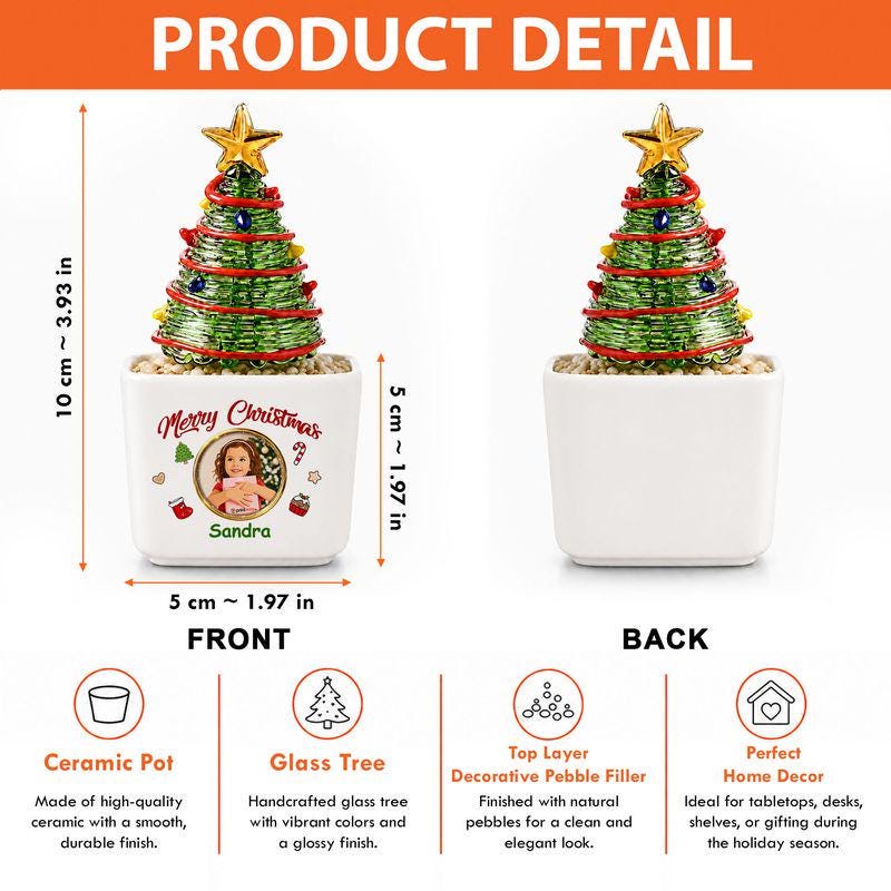 May include: A decorative glass Christmas tree with a gold star topper, sitting in a white ceramic pot. The pot features the text Merry Christmas, a circular photo, and the name Sandra. It measures 10 cm or 3.93 inches tall and 5 cm or 1.97 inches wide.