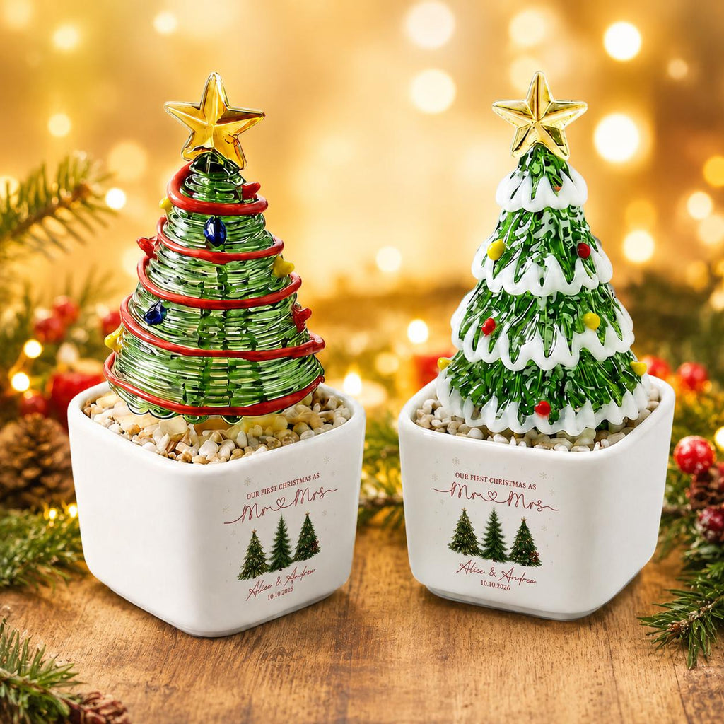 May include: Two glass Christmas tree ornaments in white square planters. The left tree has red garland and blue lights. The right tree has white snow-like accents and colorful lights. Both feature gold stars and text reading Our first Christmas as Mr & Mrs.