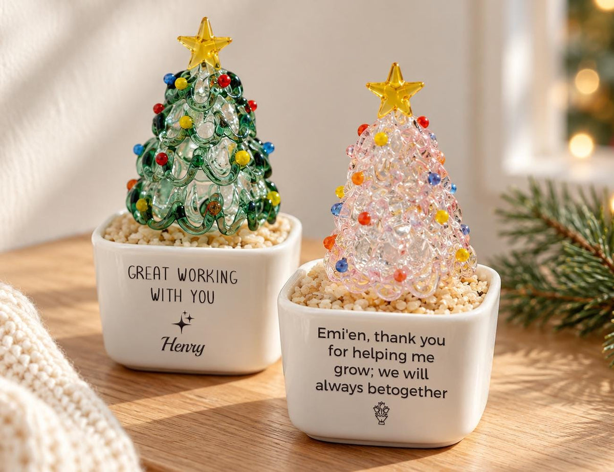 May include: Two glass Christmas tree figurines in white square ceramic planters filled with small pebbles. The left tree is green with colorful ornaments and a yellow star. The right tree is pink with colorful ornaments and a yellow star. Text reads: GREAT WORKING WITH YOU Henry and Emi'en, thank you for helping me grow; we will always betogether.