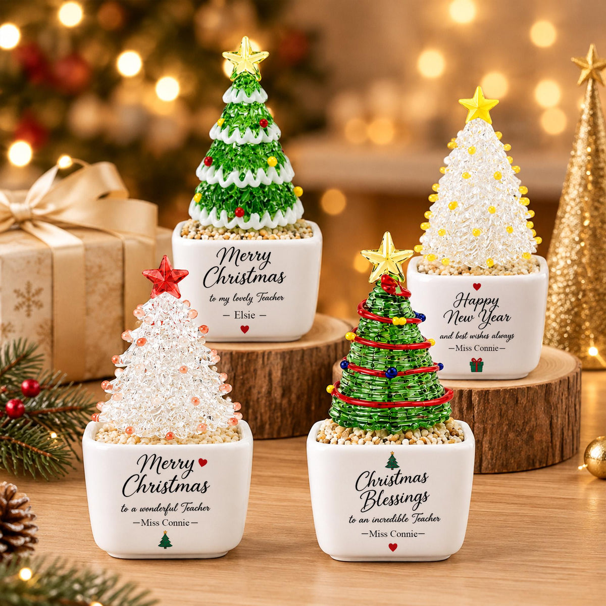 May include: Four small decorative Christmas trees in white square ceramic pots. Each tree features a star topper and colorful beads. The pots are printed with text including Merry Christmas, Happy New Year, and Christmas Blessings.