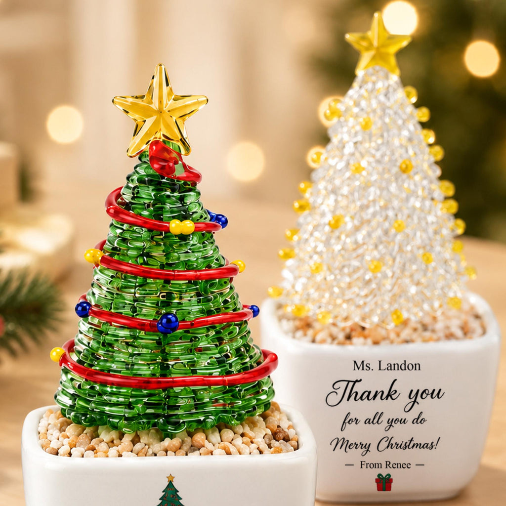 May include: Two decorative tabletop Christmas trees in white ceramic pots. The left tree is made of green wire with red garland and small blue and yellow beads, topped with a gold star. The right tree features clear beads and a gold star.