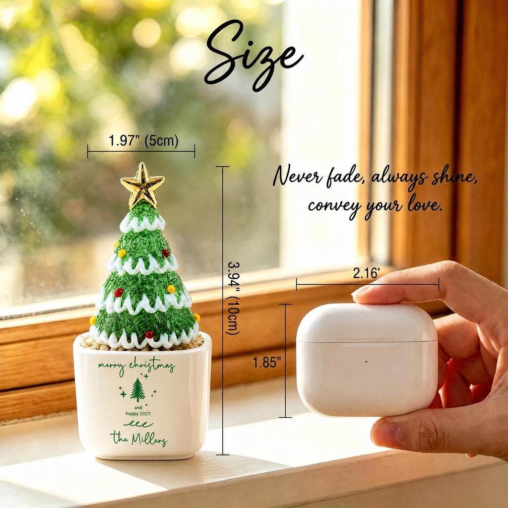 May include: A miniature green Christmas tree ornament with a gold star topper in a white ceramic pot. The pot features the text "merry christmas and happy 2027!" and "the Millers" with a tree icon. Dimensions are 1.97 inches wide and 3.94 inches tall.