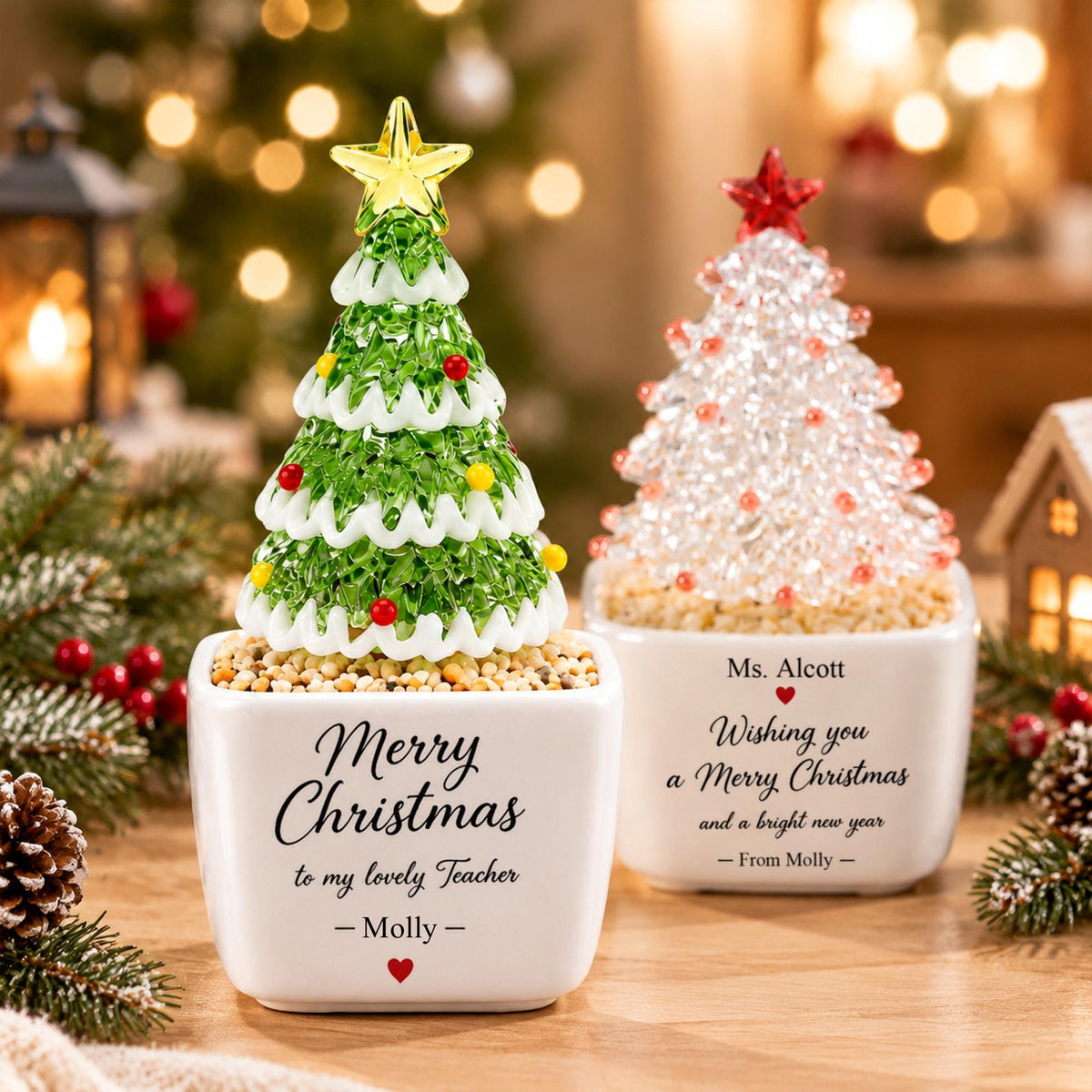 May include: Two decorative tabletop Christmas trees in white square planters. The left tree is green with yellow and red ornaments and a yellow star. The right tree is clear with red ornaments and a red star. Both feature personalized text.