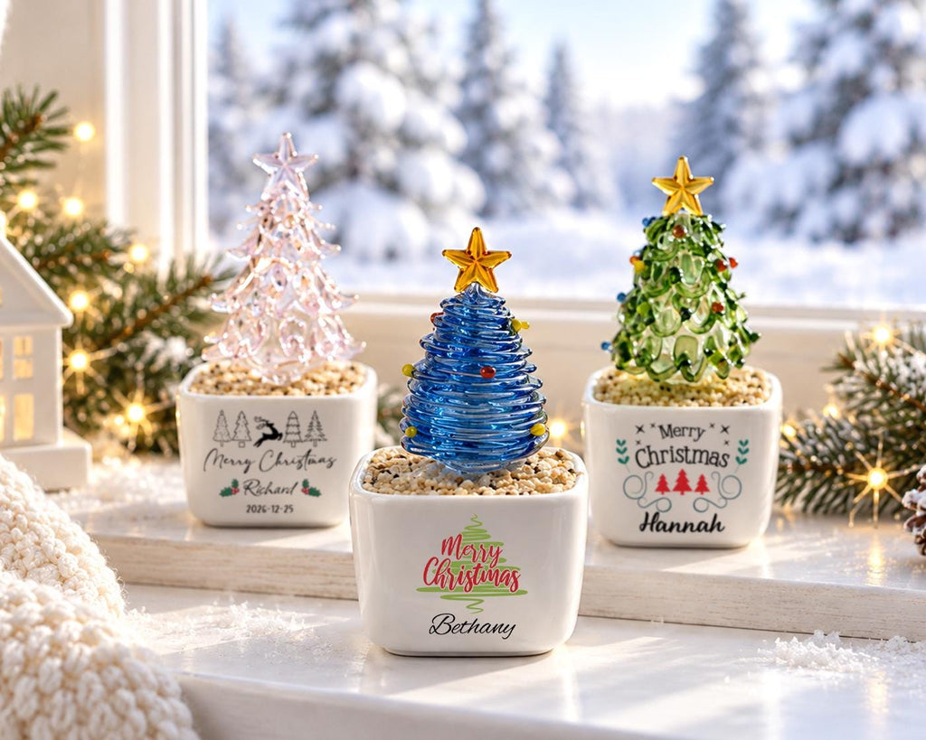 May include: Three glass Christmas tree figurines in square white ceramic pots filled with small stones. The left pot features a reindeer and "Merry Christmas Richard 2026-12-25". The center pot has "Merry Christmas Bethany". The right pot has "Merry Christmas Hannah".