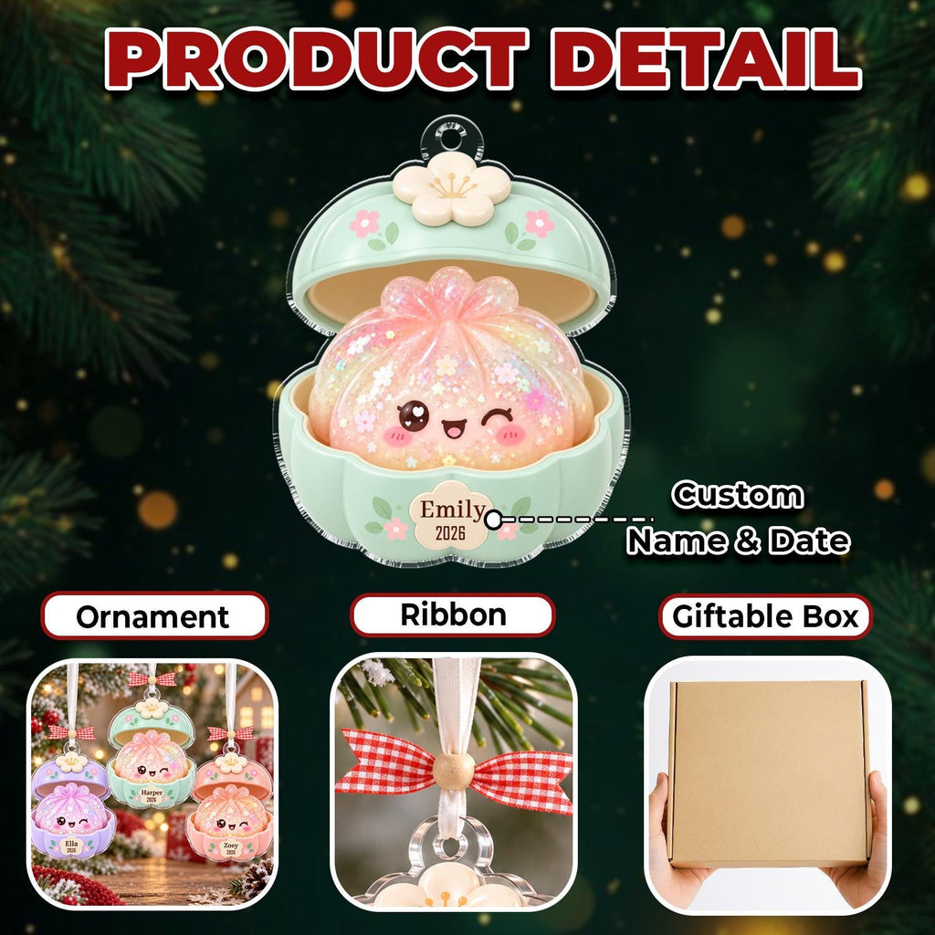 May include: A pastel green clam-shaped ornament containing a glittery, iridescent, smiling dumpling character with a wink. The exterior features a white flower topper and a custom name and date label. Includes a red and white gingham ribbon and box.
