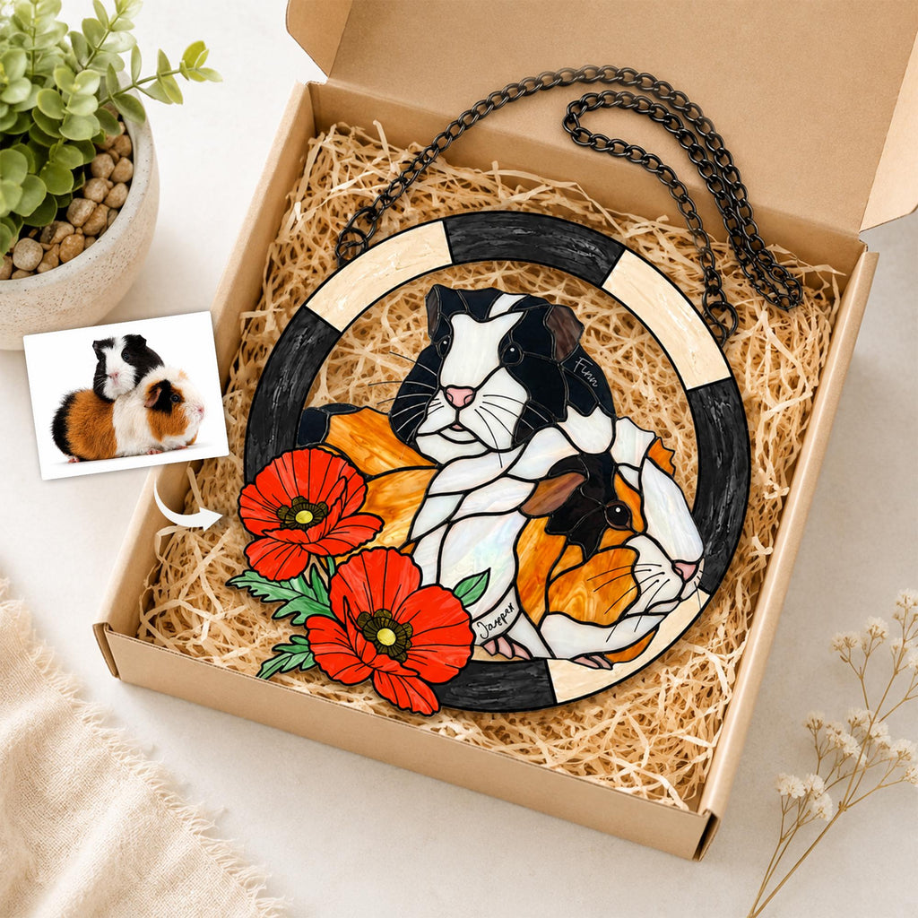 May include: A circular stained glass suncatcher featuring two guinea pigs, one black and white and one orange and white, surrounded by red poppy flowers. The piece is framed by a black and cream border and includes a black metal hanging chain.