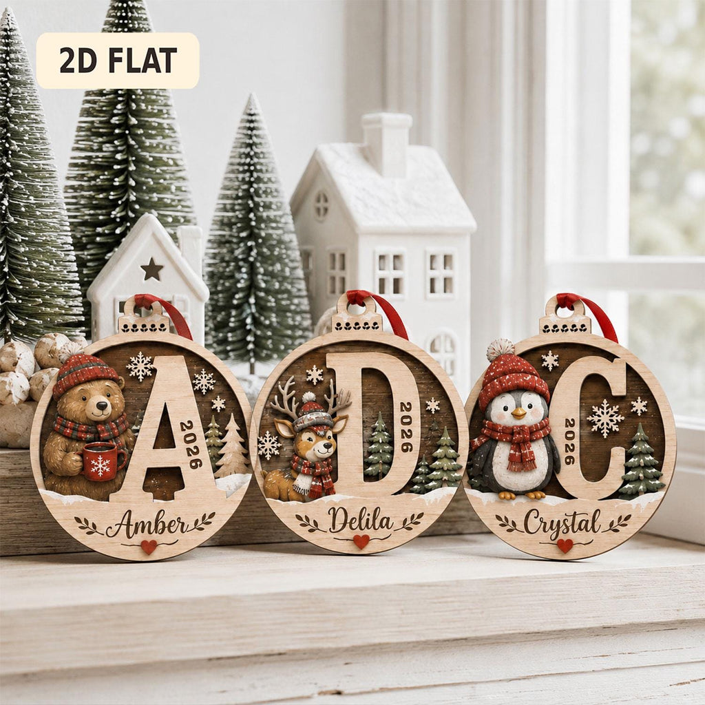 May include: Three round wooden Christmas ornaments featuring the letters A, D, and C. Each ornament displays a winter animal: a bear, a deer, and a penguin, all wearing red hats and scarves. The text 2026, snowflakes, and names Amber, Delila, and Crystal are visible.
