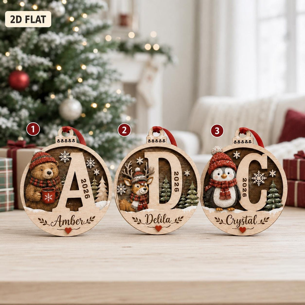 May include: Three circular wooden Christmas ornaments featuring a bear, a deer, and a penguin, each wearing a red winter hat and scarf. The ornaments display the letters A, D, and C, the year 2026, and the names Amber, Delila, and Crystal.