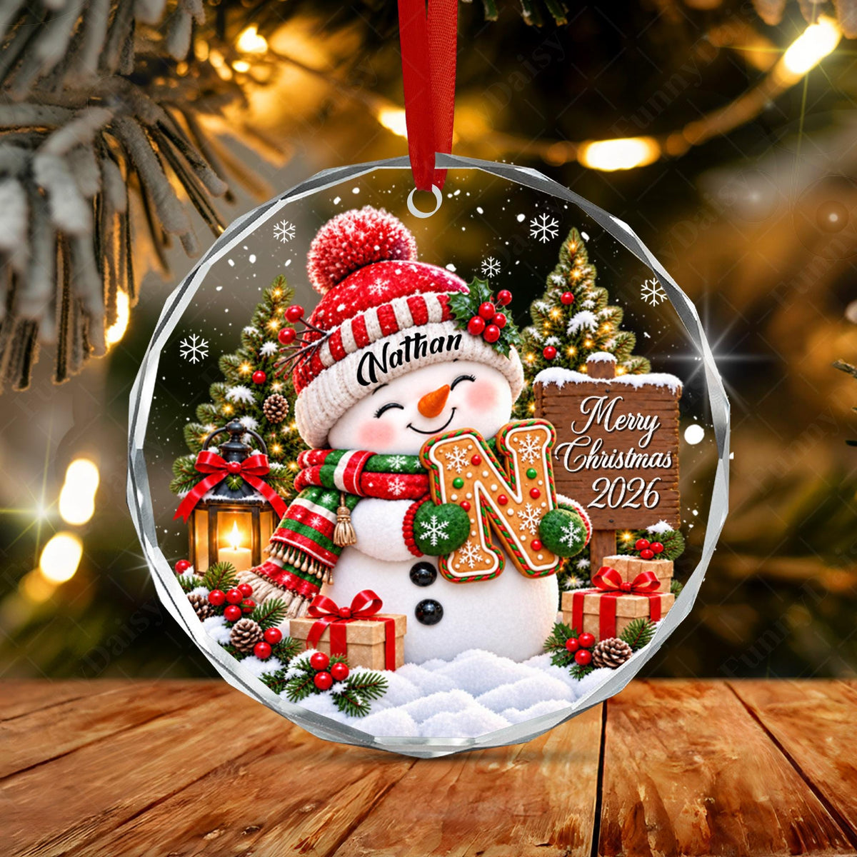 May include: A round, clear acrylic Christmas ornament featuring a snowman wearing a red hat with the name Nathan, a red and green scarf, and holding a large letter N. The design includes a wooden sign reading Merry Christmas 2026.