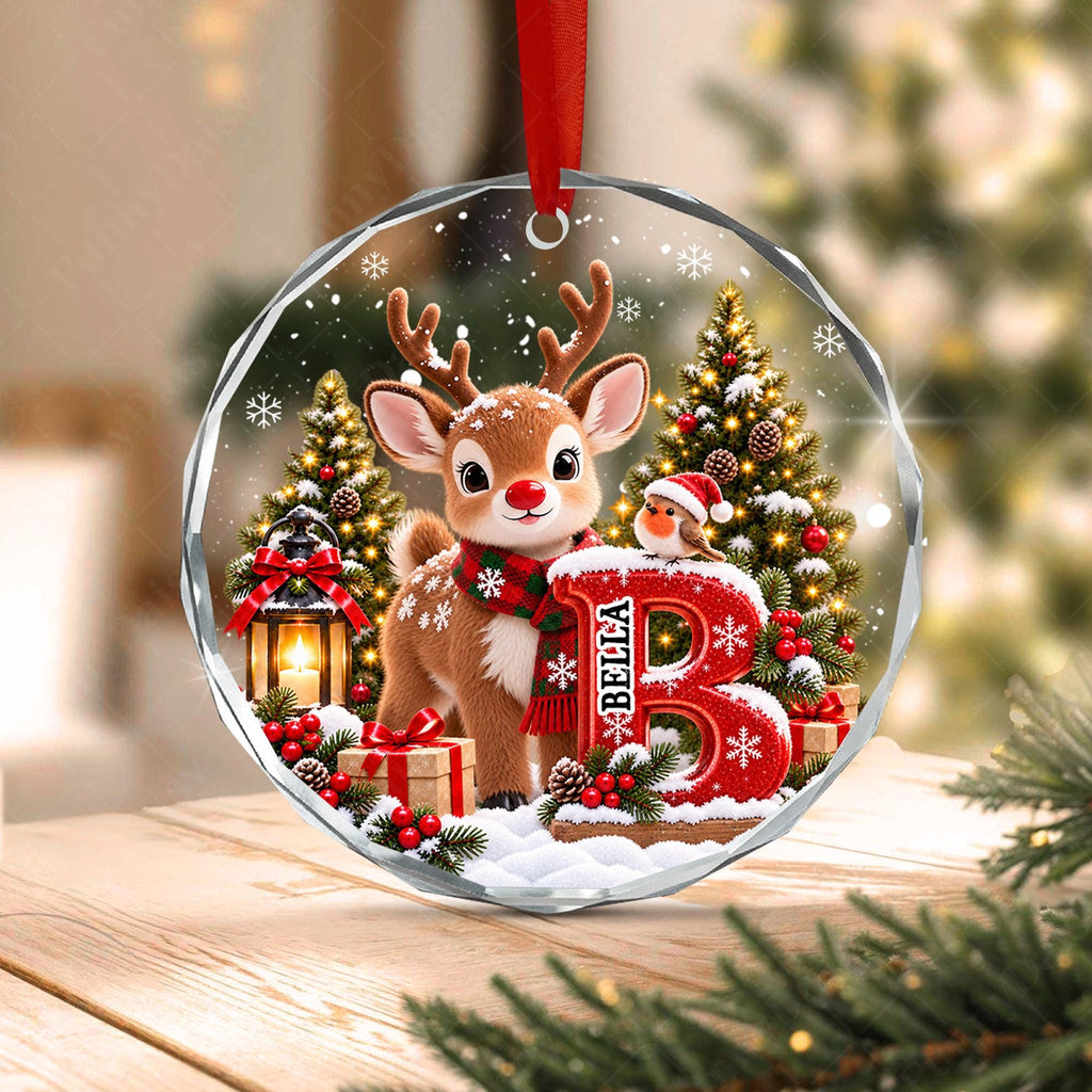 May include: A round, clear acrylic Christmas ornament featuring a printed illustration of a brown reindeer wearing a red and green plaid scarf, standing next to a large red letter B with the name Bella, a small bird, and a lantern.