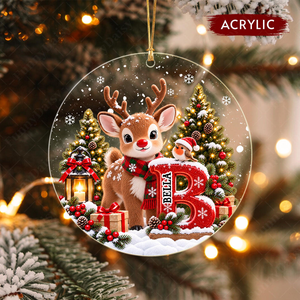 May include: A round acrylic Christmas ornament featuring a brown reindeer wearing a red and green plaid scarf, standing next to a large red letter B with the name BELLA printed on it. The scene includes a lantern, a small bird, and pine trees.