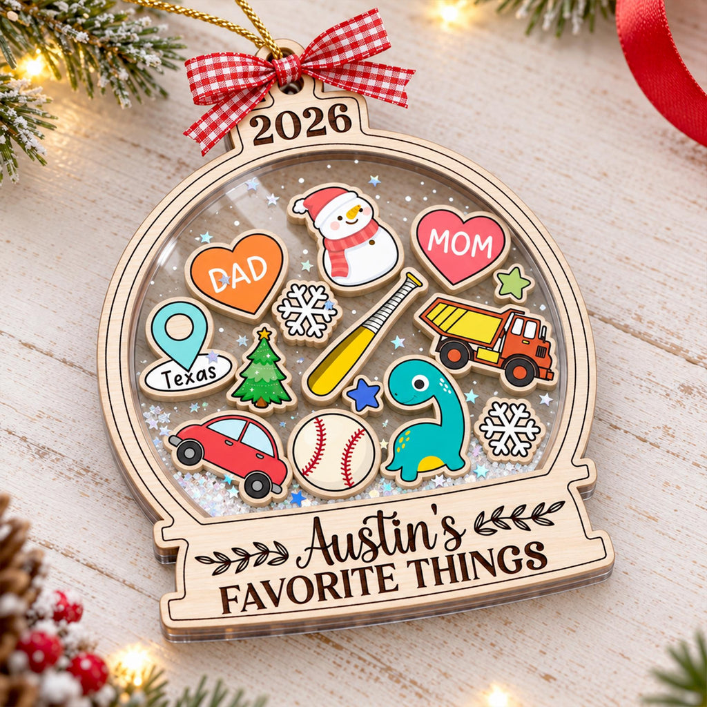 May include: A wooden snow globe ornament featuring the year 2026, a red and white gingham bow, and the text Austin's FAVORITE THINGS. Inside are colorful icons including a snowman, hearts labeled DAD and MOM, a truck, dinosaur, and baseball.