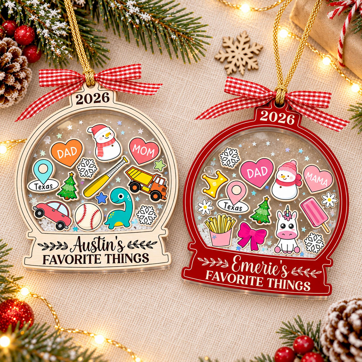 May include: Two globe-shaped Christmas ornaments with gold hanging cords and red gingham bows. The left ornament is light wood with '2026' and 'Austin's FAVORITE THINGS' text, featuring icons like a snowman, truck, and baseball. The right is red with '2026' and 'Emerie's FAVORITE THINGS' text, featuring a unicorn, fries, and snowman.