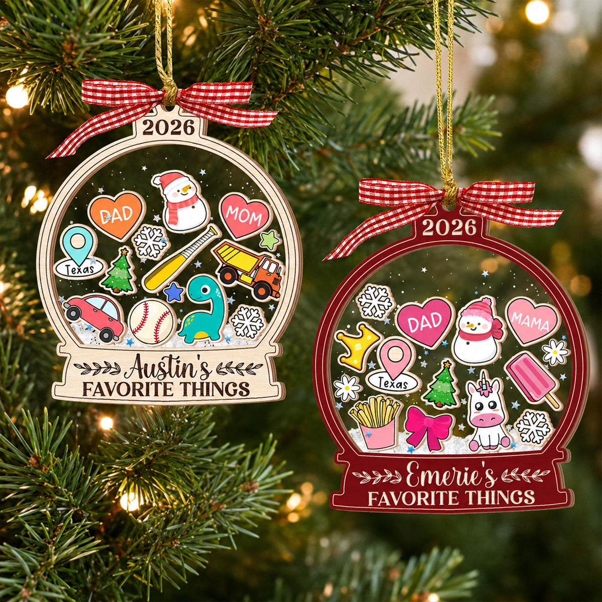 May include: Two snow globe-shaped Christmas ornaments with red and white gingham bows. The left ornament says 2026 and Austin's FAVORITE THINGS with icons of a snowman, hearts, baseball, truck, and car. The right says 2026 and Emerie's FAVORITE THINGS with a unicorn, snowman, hearts, and fries.