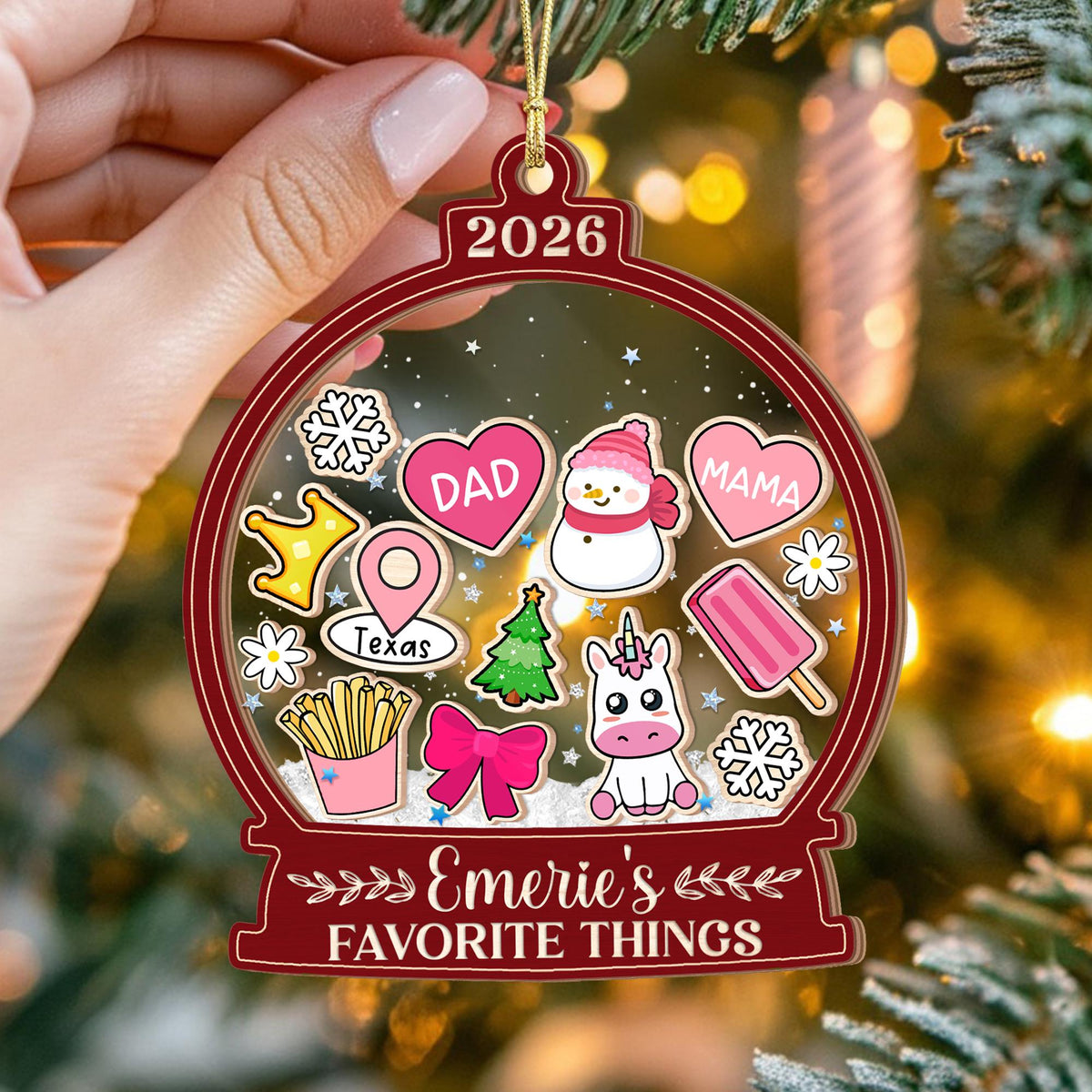 May include: A flat, globe-shaped Christmas ornament with a dark red border and the year 2026 at the top. The center features various colorful icons including hearts labeled DAD and MAMA, a snowman, a unicorn, fries, and text reading Emerie's FAVORITE THINGS.