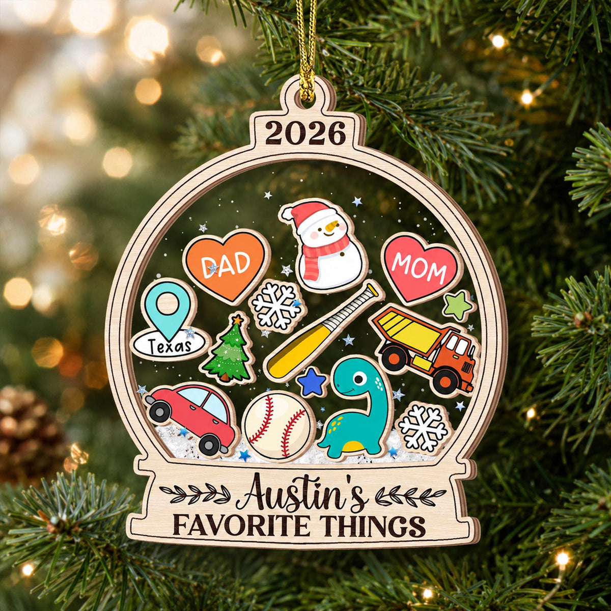 May include: A wooden snow globe ornament featuring the year 2026 at the top and the text Austin's FAVORITE THINGS at the bottom. The center contains colorful illustrations of a snowman, hearts labeled DAD and MOM, a Texas map pin, a baseball bat, a dump truck, a car, a dinosaur, a Christmas tree, snowflakes, and a baseball.