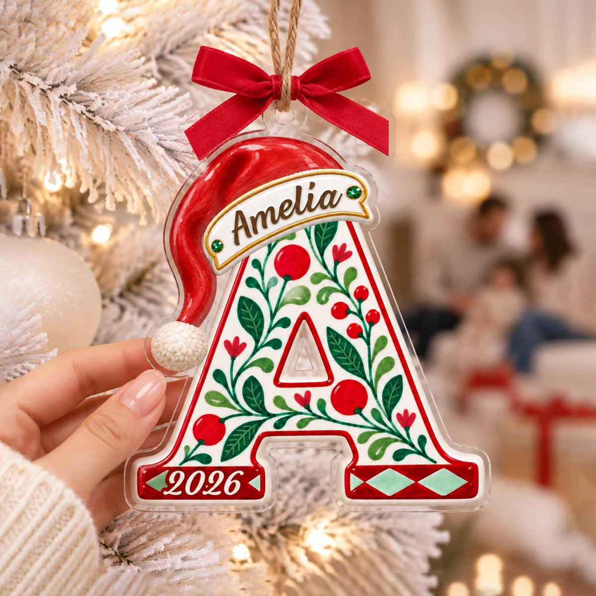 May include: A clear acrylic Christmas ornament shaped like the letter A, topped with a red ribbon bow and a red Santa hat. The letter features green holly leaves, red berries, the name Amelia, and the year 2026 printed in red and green.