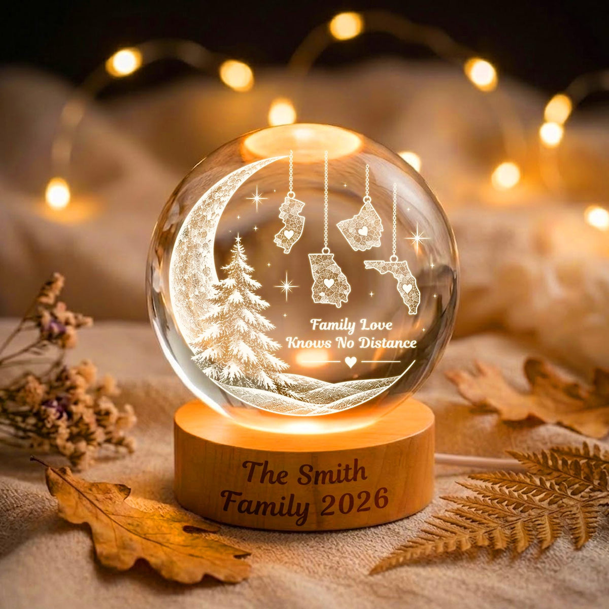 May include: A clear glass sphere lamp on a round wooden base engraved with The Smith Family 2026. The sphere features an etched crescent moon, a pine tree, and four US state shapes hanging from strings with the text Family Love Knows No Distance.
