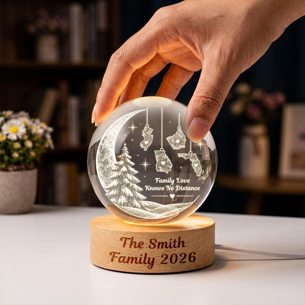 May include: A clear glass sphere night light featuring an etched crescent moon, a pine tree, and four US state shapes hanging from chains. The text reads Family Love Knows No Distance. The light sits on a round wooden base engraved with The Smith Family 2026.