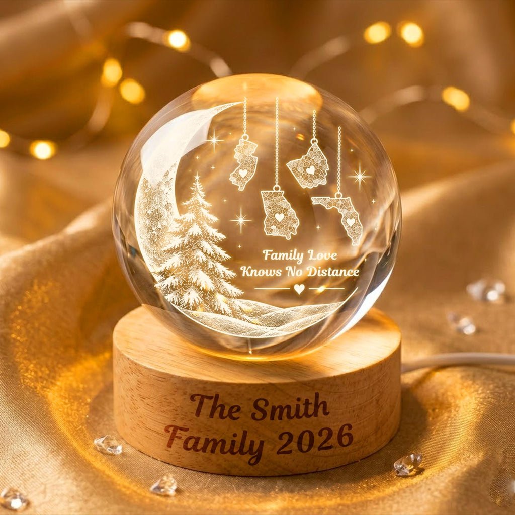 May include: A clear glass sphere featuring an internal laser-etched design of a crescent moon, a pine tree, and four US state maps with hearts. The text reads Family Love Knows No Distance. It sits on a wooden base engraved with The Smith Family 2026.