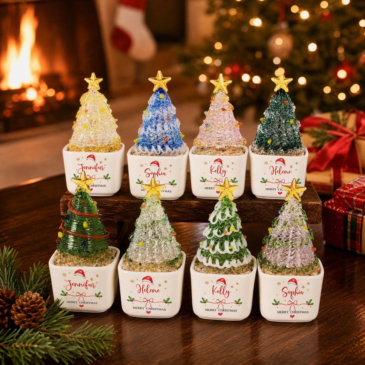 May include: Eight small decorative Christmas trees in white square ceramic pots. Each tree features a unique color and texture, topped with a gold star. The pots are printed with names like Jennifer, Sophia, Kelly, and Helene, plus Merry Christmas.