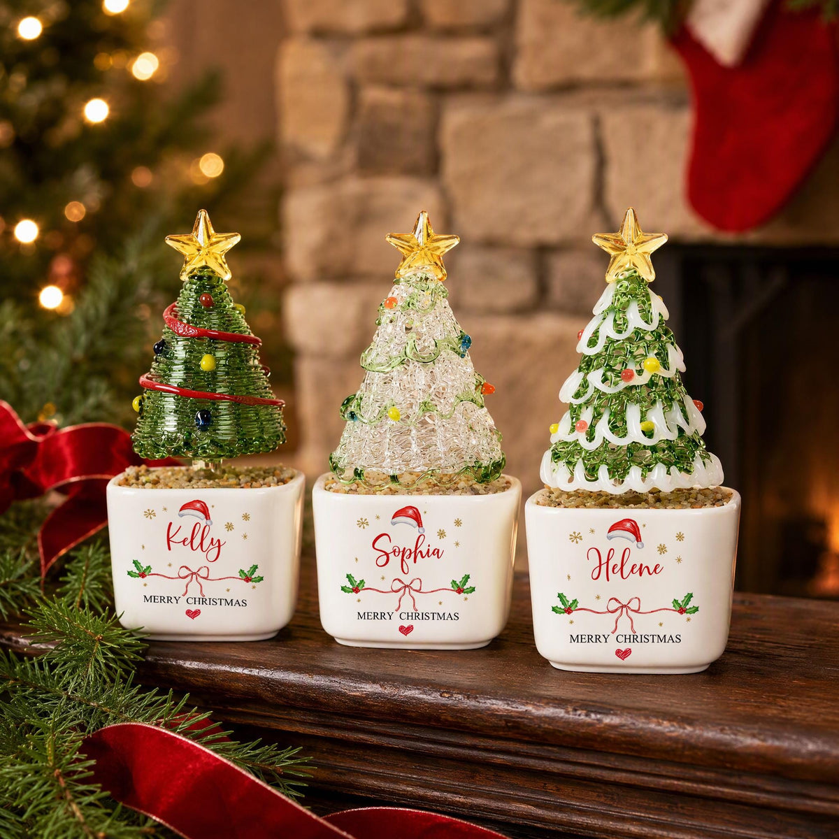 May include: Three decorative tabletop Christmas trees in square white ceramic pots. Each tree is topped with a gold star and features personalized names Kelly, Sophia, and Helene printed in red script above Merry Christmas text.