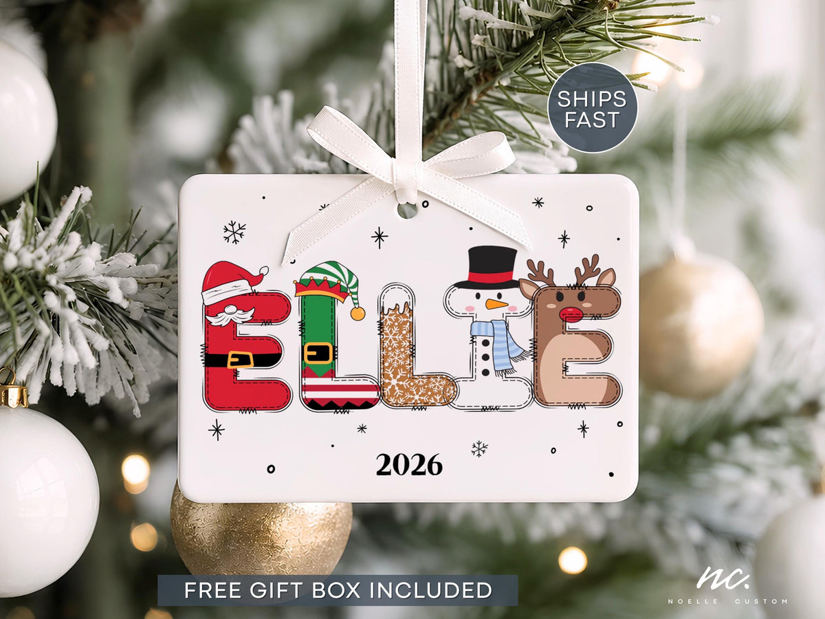 May include: A rectangular white ceramic Christmas ornament featuring the name ELLIE spelled out in festive holiday characters including a Santa suit, an elf outfit, a gingerbread pattern, a snowman, and a reindeer. The year 2026 is printed below.