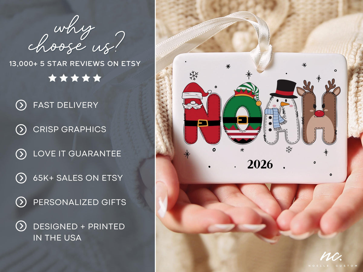 May include: A rectangular white ceramic Christmas ornament featuring the name NOAH in festive character-themed letters, including a Santa suit, elf hat, snowman, and reindeer. The year 2026 is printed below the name, and a white ribbon is attached.