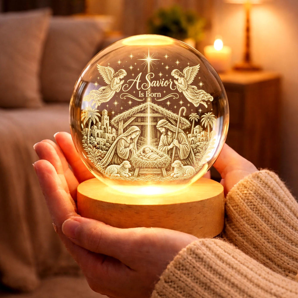 May include: A clear glass sphere night light featuring an internal laser-etched nativity scene with the text A Savior Is Born, two angels, and a star. The sphere rests on a circular light-up wooden base that illuminates the detailed religious design.