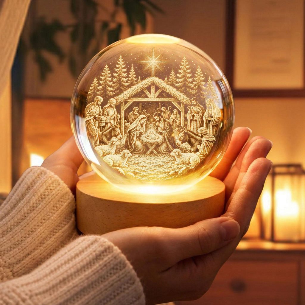 May include: A clear glass sphere featuring a laser-etched nativity scene with a star, trees, and figures, illuminated from below by a round, light-colored wooden base. The internal design depicts a stable, animals, and people surrounding a manger.
