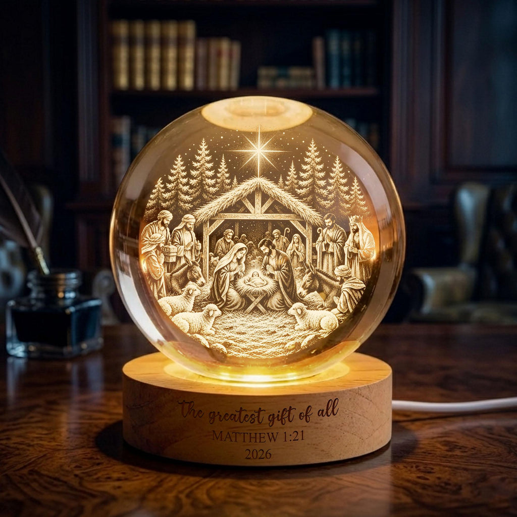 May include: A spherical glass ornament featuring an internal laser-etched nativity scene with a star, trees, and figures, illuminated from below by a circular wooden base engraved with the text The greatest gift of all MATTHEW 1:21 2026.