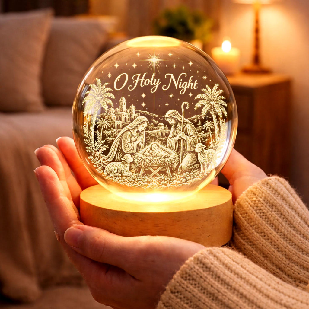 May include: A spherical glass ornament featuring an engraved nativity scene with the text O Holy Night, a star, palm trees, and figures surrounding a manger. The clear glass sphere rests on a circular light-colored wooden base that illuminates.