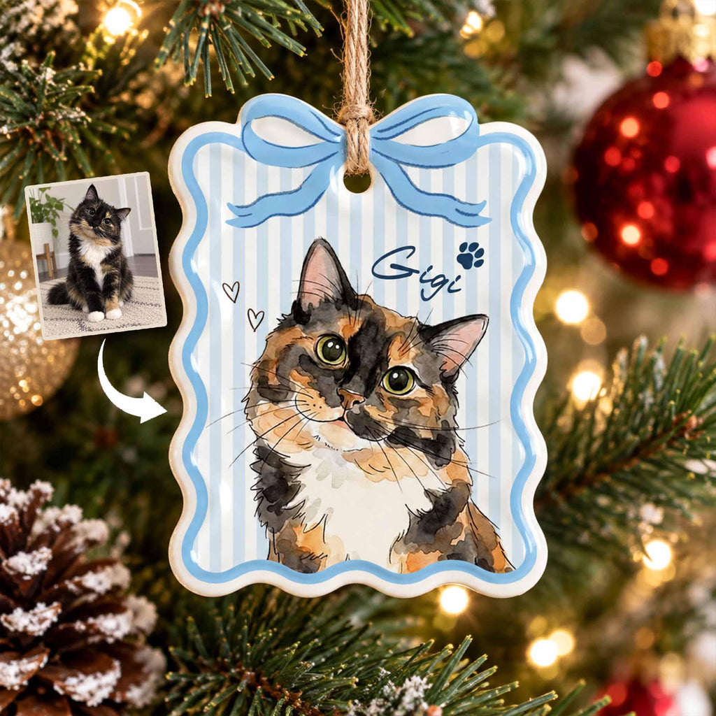 May include: A rectangular ceramic ornament with scalloped edges and a light blue striped pattern. It features a watercolor-style illustration of a calico cat, the name Gigi in script, a paw print, and two small hearts. A jute twine loop is attached.