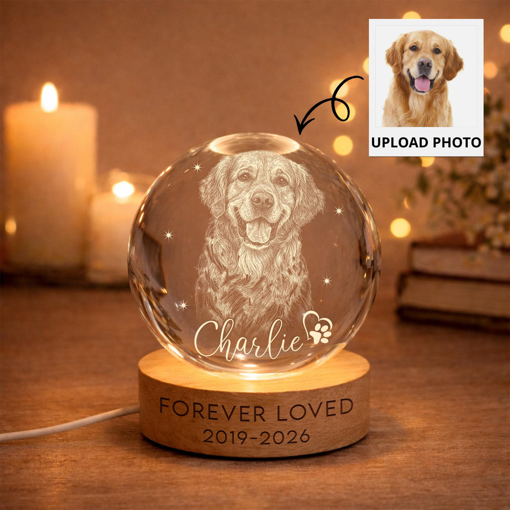 May include: A clear glass sphere featuring an etched portrait of a golden retriever dog, the name Charlie, and a paw print icon. The sphere rests on a circular wooden base engraved with the text FOREVER LOVED and the years 2019-2026.