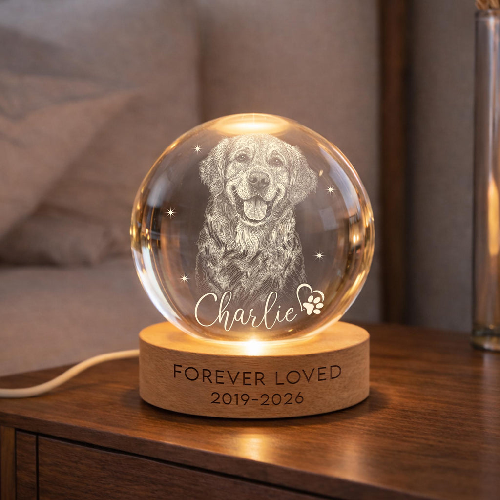May include: A clear glass sphere lamp featuring an etched portrait of a dog, the name Charlie, and a paw print heart. The sphere rests on a round wooden base engraved with the text FOREVER LOVED and the years 2019-2026, illuminated from below.