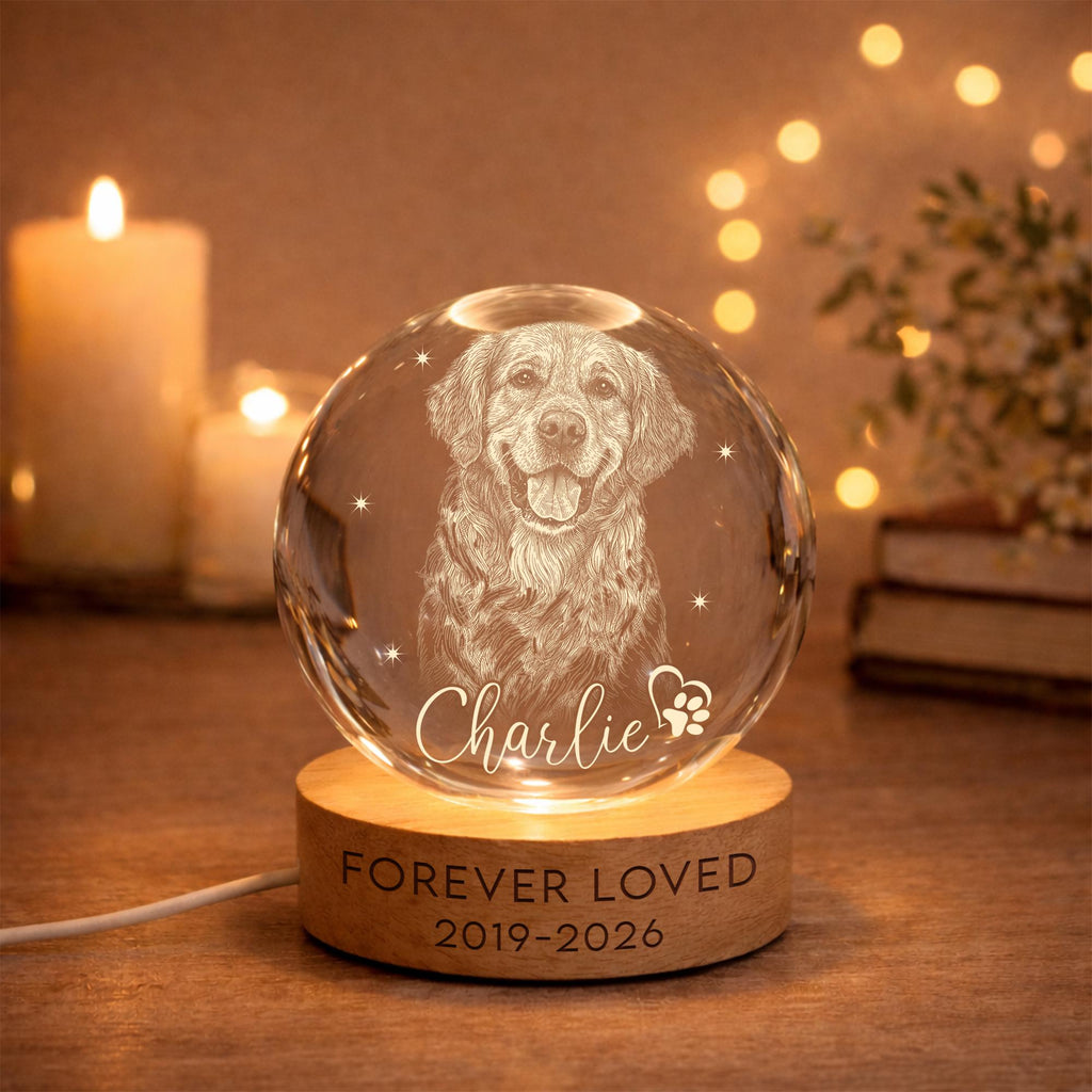 May include: A clear glass sphere featuring an etched portrait of a dog, the name Charlie, and a paw print heart. The sphere rests on a round wooden base engraved with the text FOREVER LOVED and the years 2019-2026, illuminated from below.