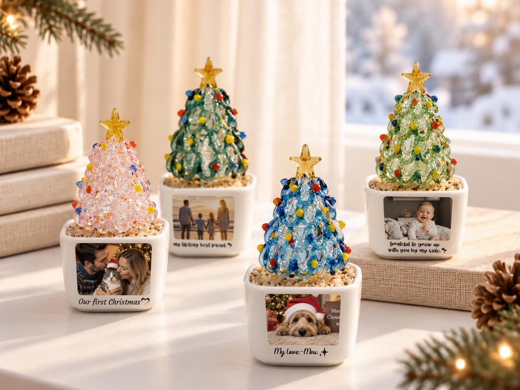 May include: Four decorative glass Christmas tree ornaments in white square ceramic planters. Each tree features colorful glass beads and a yellow star topper. The planters display personalized photographs and text, including Our first Christmas.