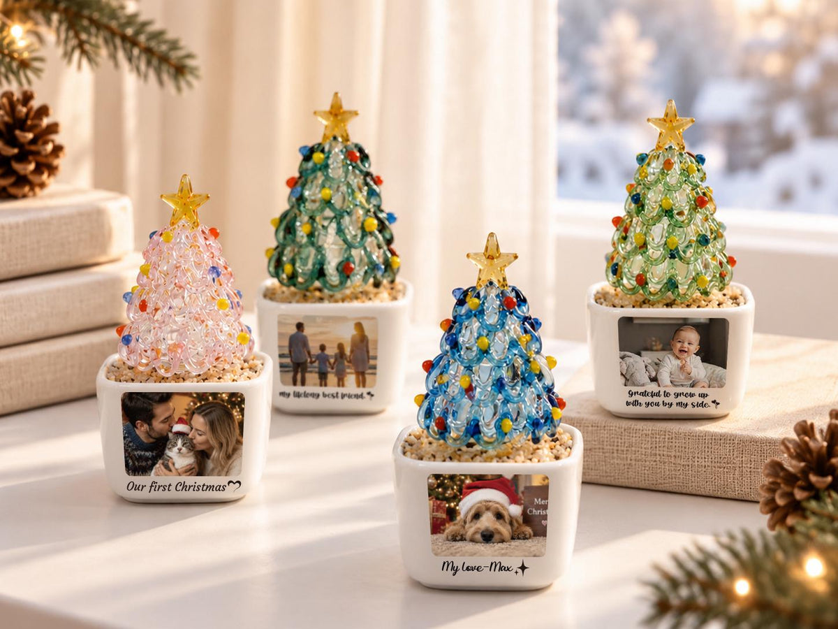 May include: Four decorative glass Christmas tree ornaments in white square ceramic planters. Each tree features colorful glass beads and a yellow star topper. The planters display personalized photographs and text, including Our first Christmas.